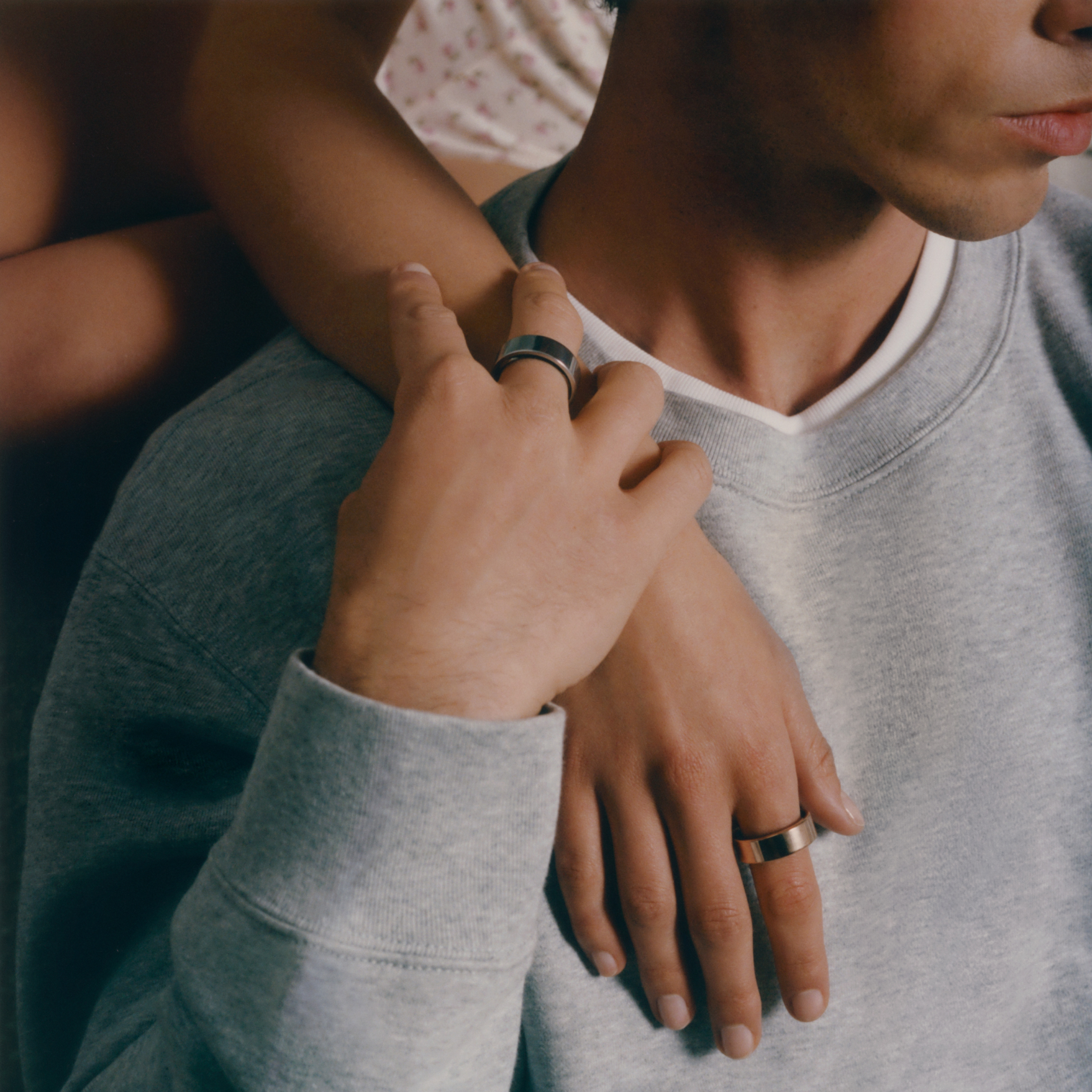 Two people holding hands with visible rings, wearing gray shirts.